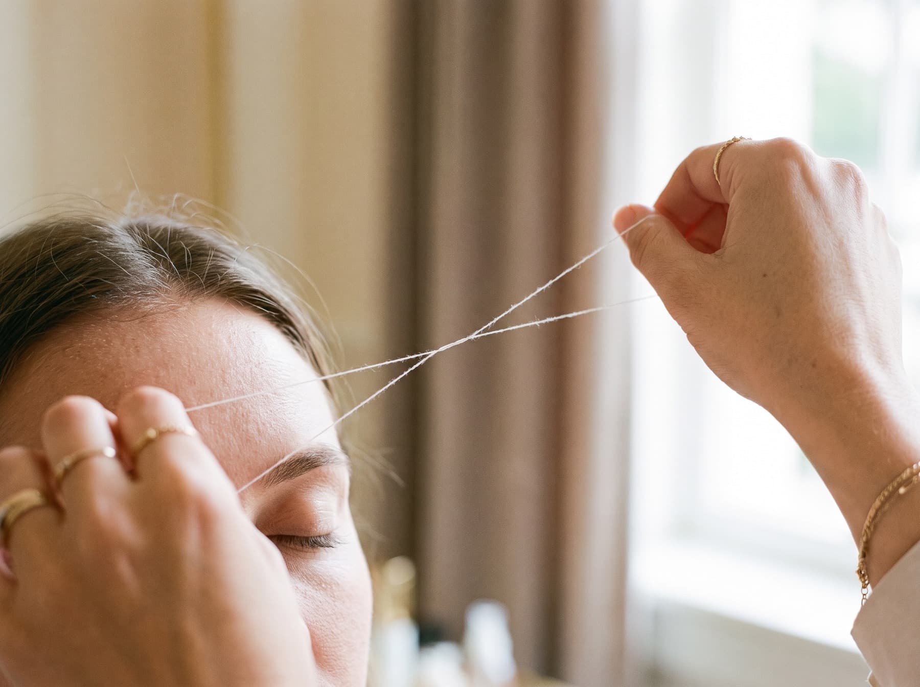A technician holding a twisted cotton thread taut against a client's brow line while shaping the eyebrow.